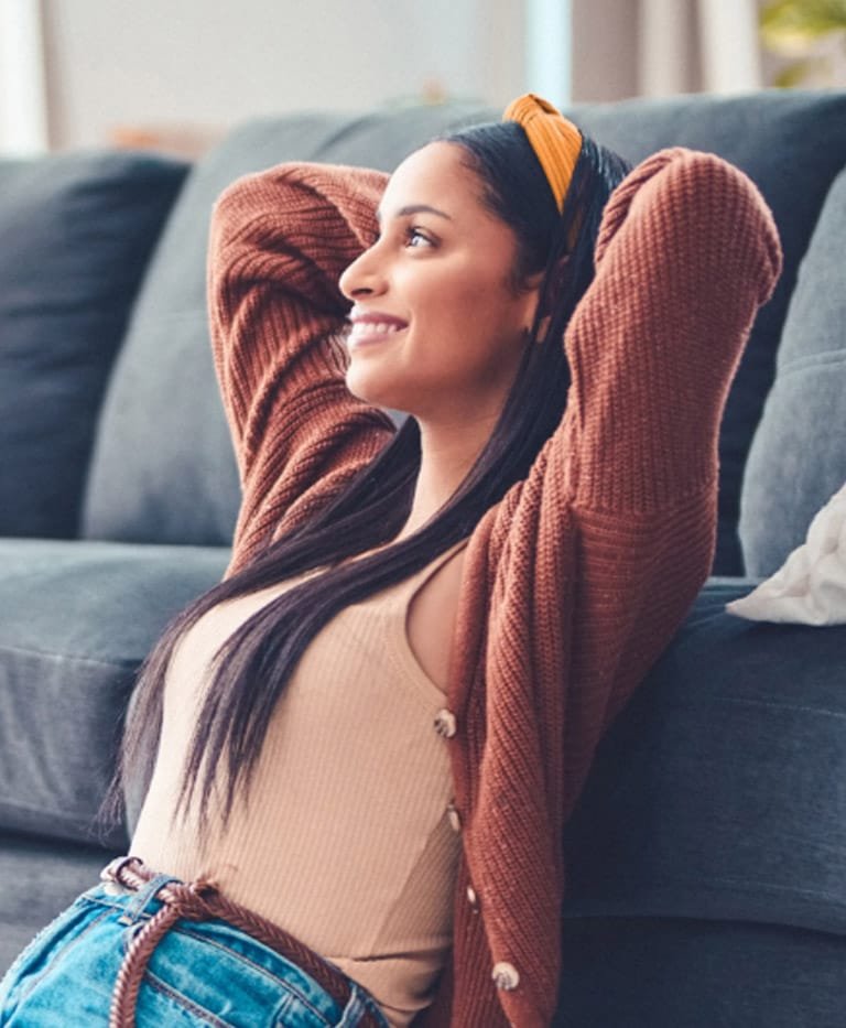 Woman leaning back against a couch with her hands behind her head