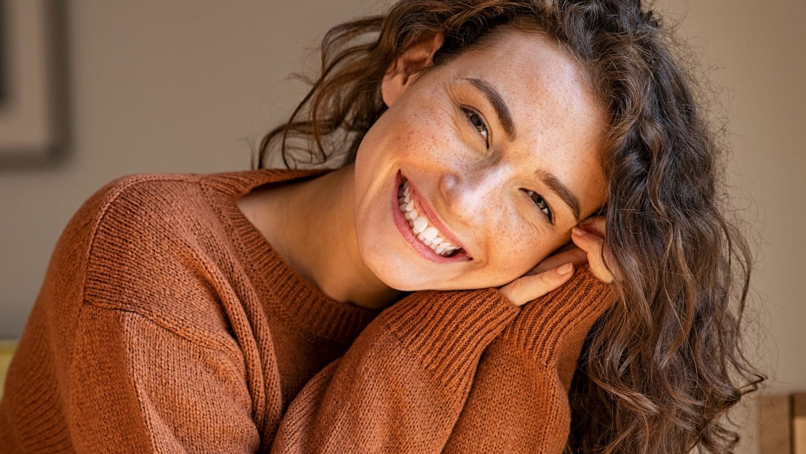 Woman with curly hair smiling, resting her face on her hands