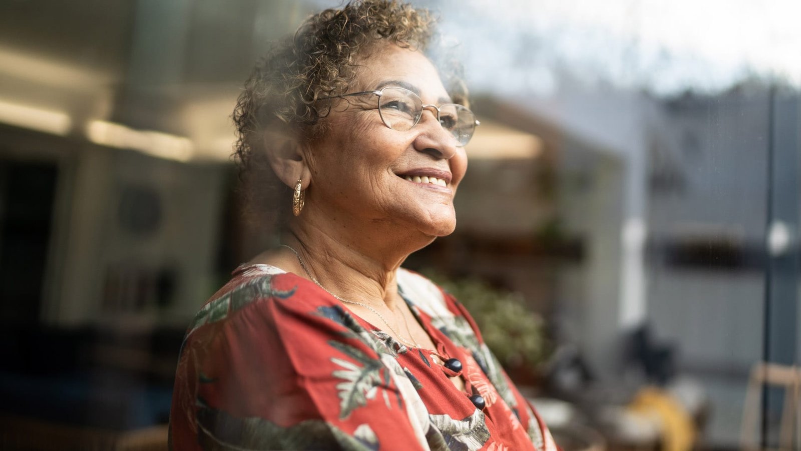 Older woman smiling, looking out a window